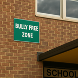 Green 'Bully Free Zone' sign on a brick wall next to a school building.